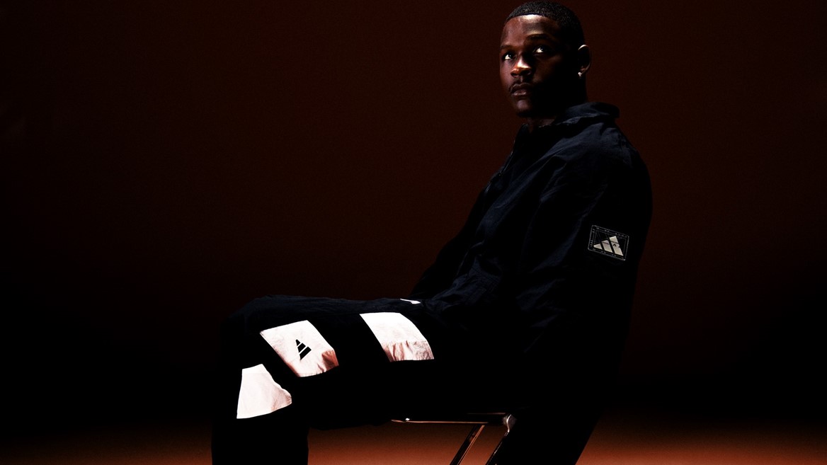 Anthony Edwards assis en tenue adidas noire dans le visuel officiel de sa troisième chaussure signature.